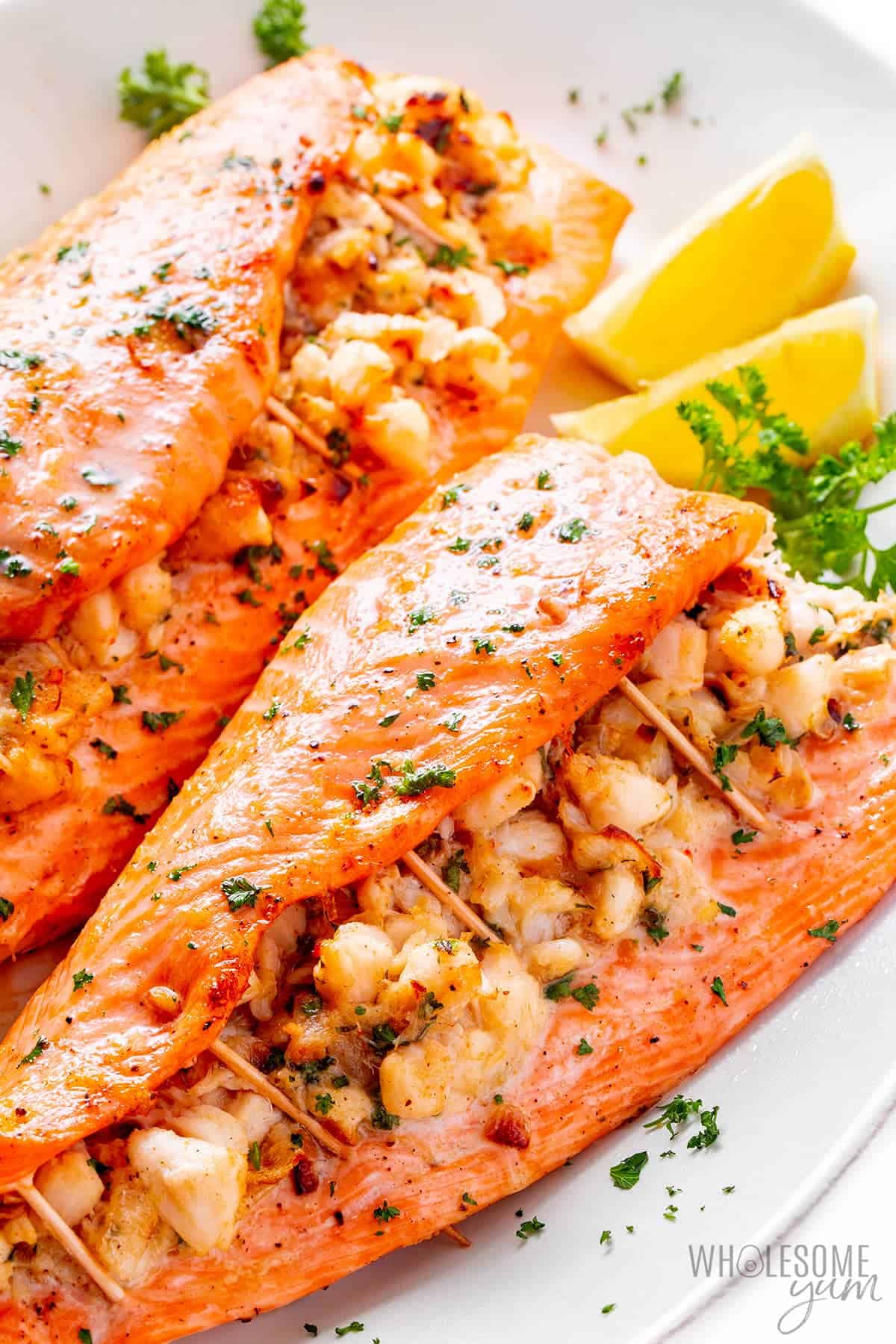 Crab stuffed salmon recipe on a platter with lemon wedges.