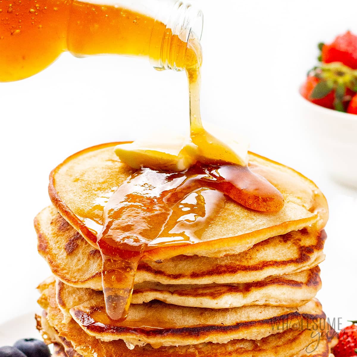 Keto sugar free maple syrup pouring onto stack of pancakes.