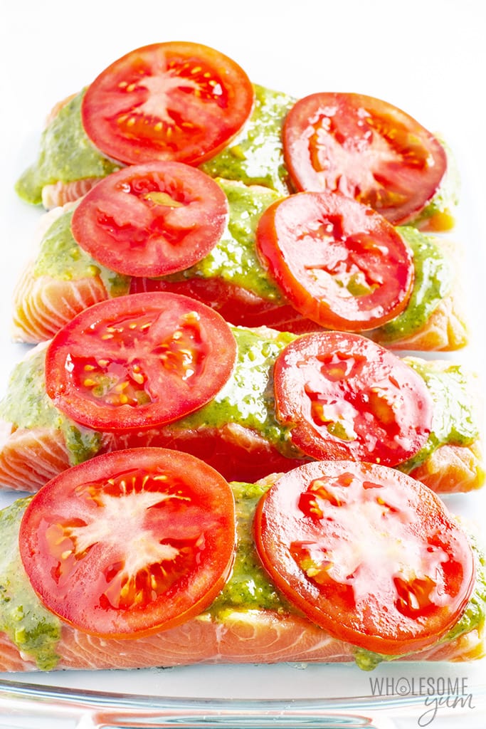 Raw salmon filets with basil pesto in a baking dish topped with tomato slices