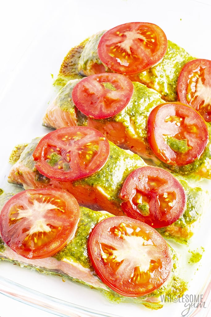 Salmon filets with basil pesto in a baking dish topped with tomato slices