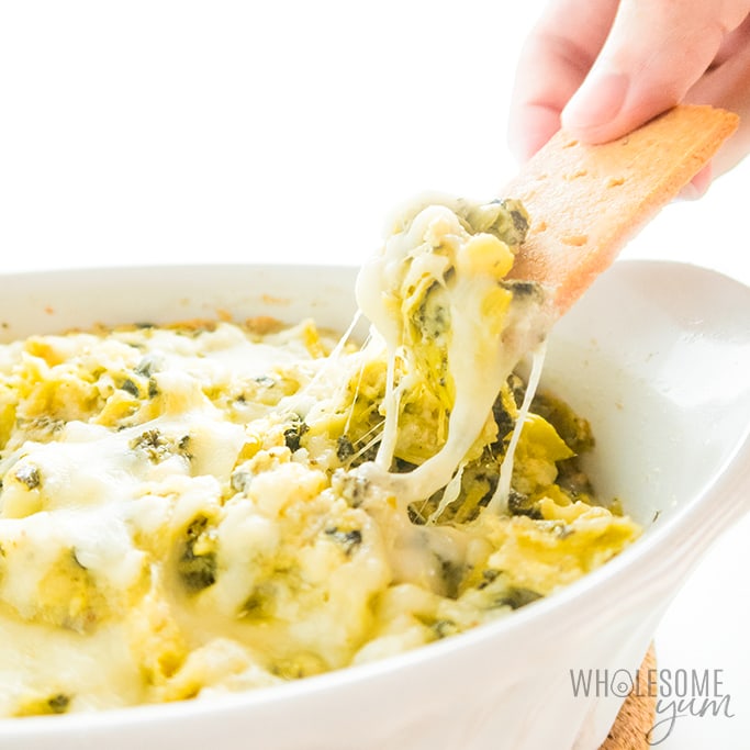 cheesy spinach artichoke dip with cracker dipping into it