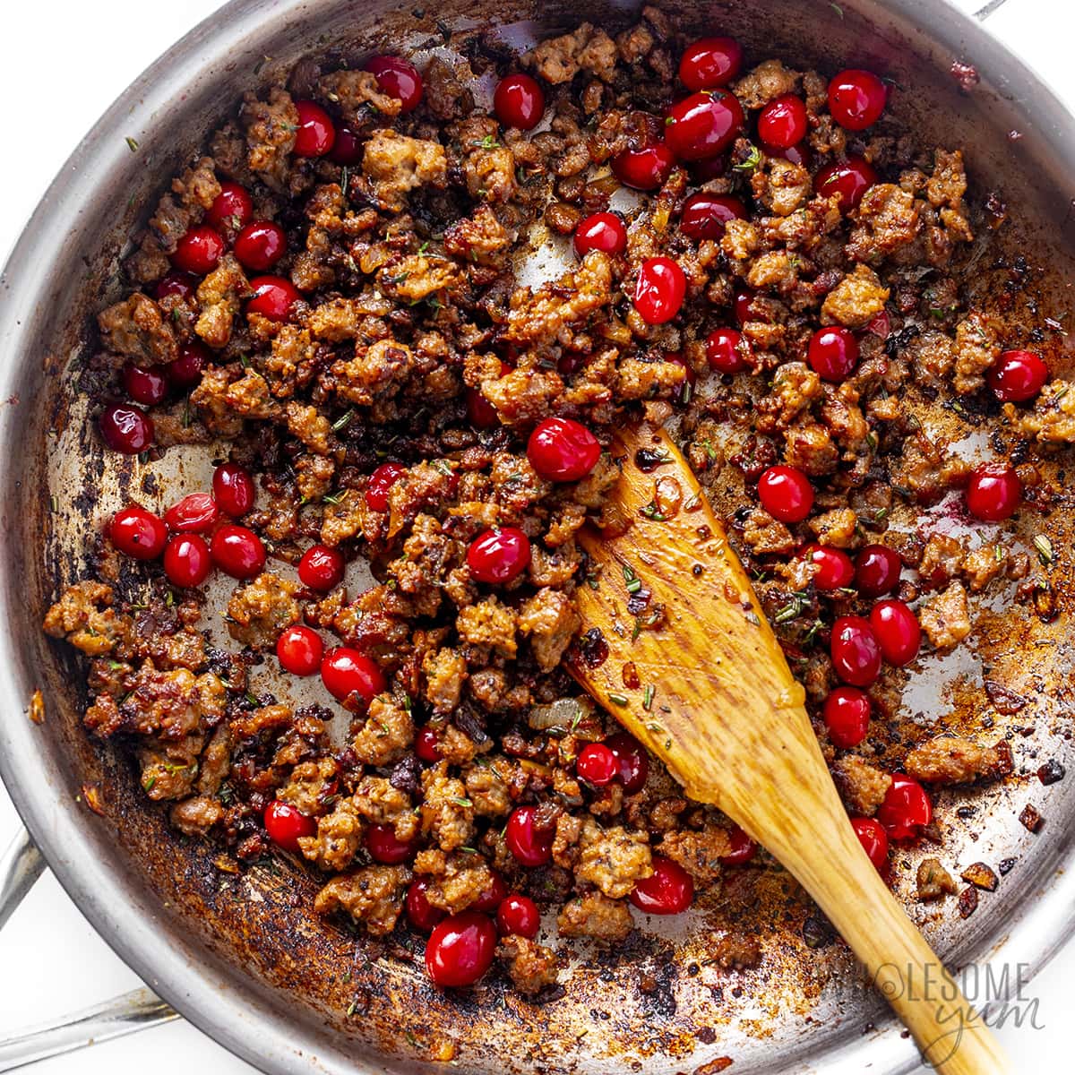 Cranberries and herbs added to sausage in a skillet.
