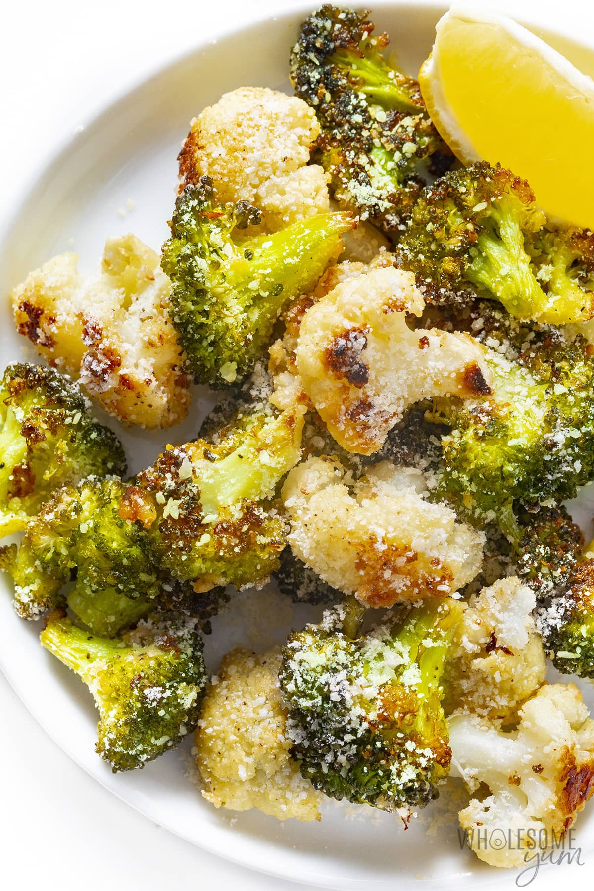Parmesan cauliflower and broccoli on a plate with lemon wedge.