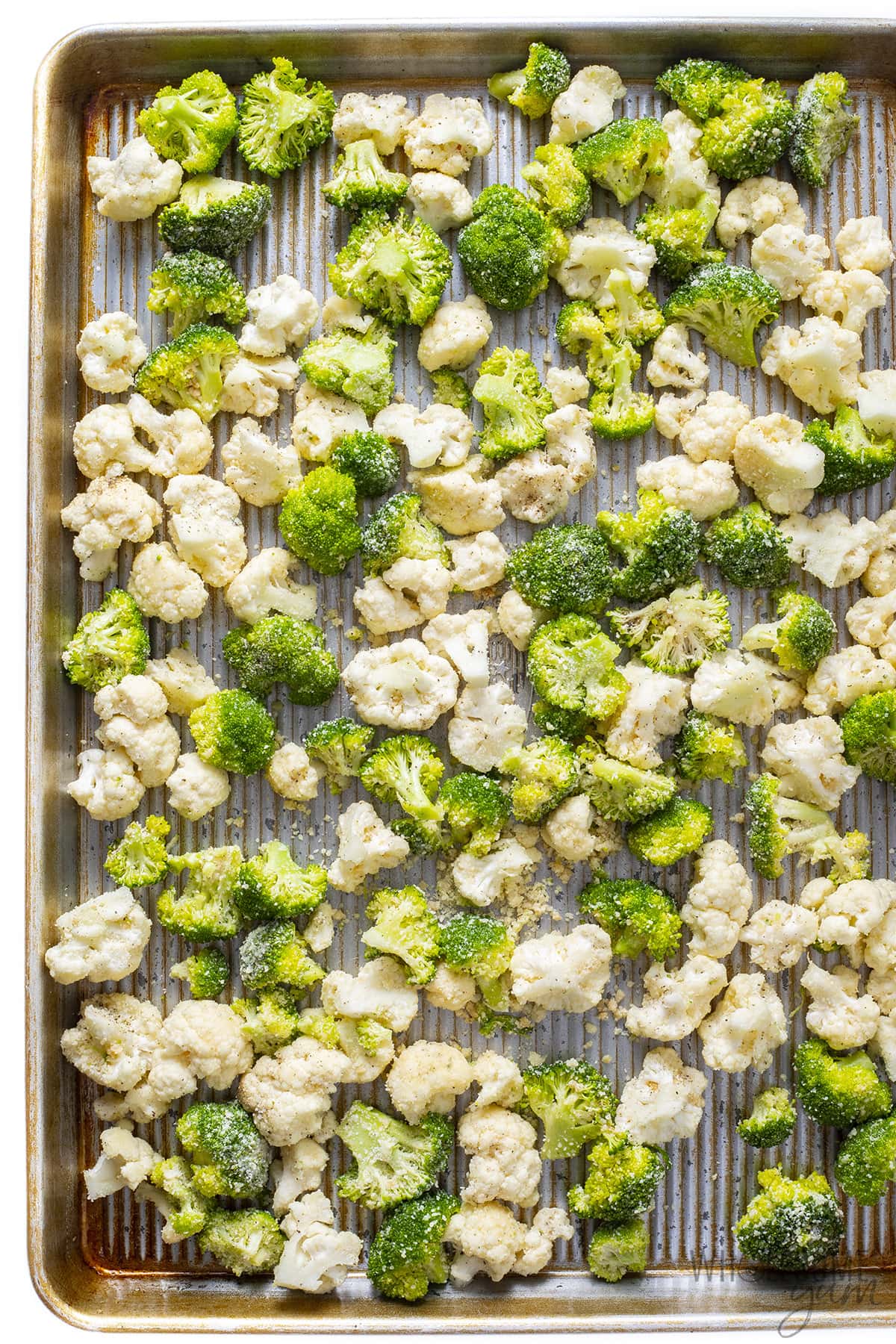 Raw cauliflower and broccoli spread out on a sheet pan.