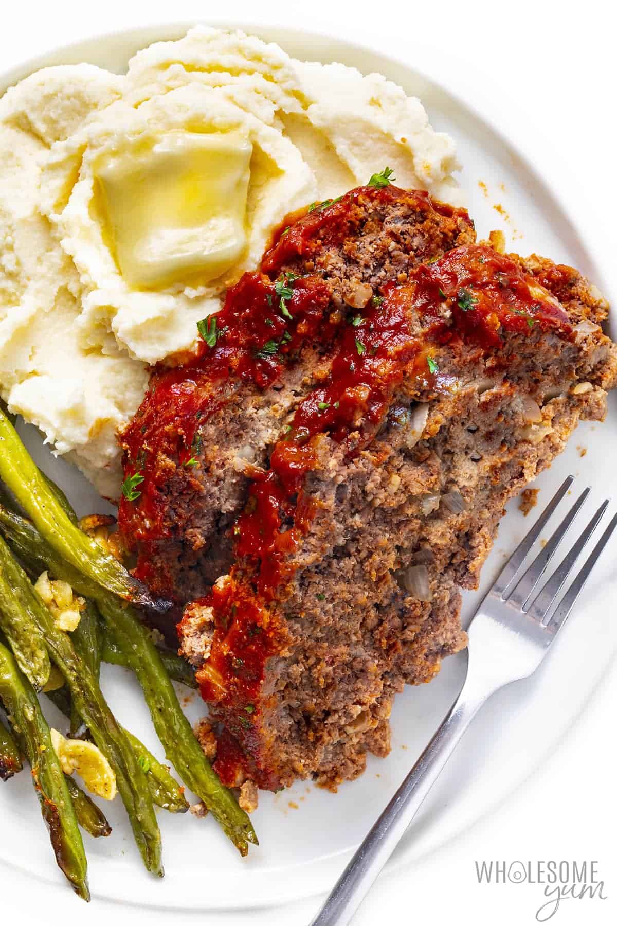 Slices of keto friendly meatloaf with green beans and mashed cauliflower.