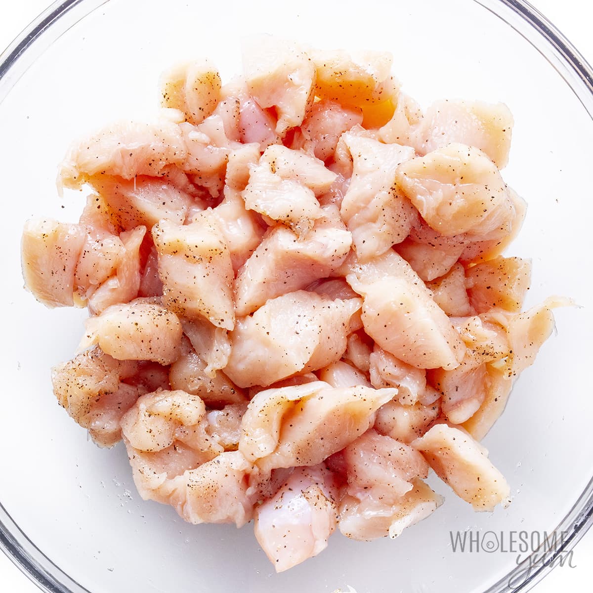 Chicken pieces in a bowl seasoned with salt and pepper.