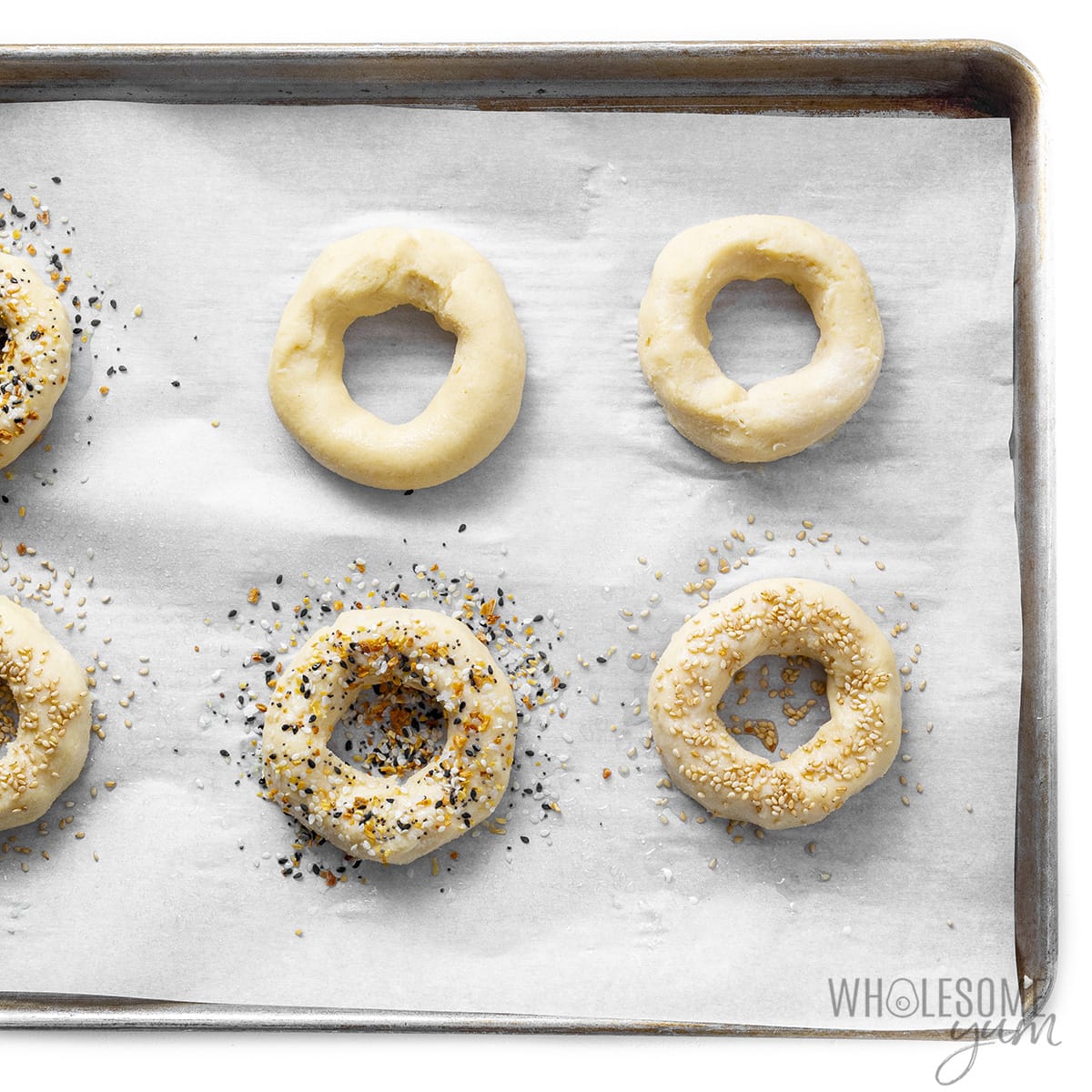 Raw keto bagel recipe dough sprinkled with toppings on a lined baking sheet. 