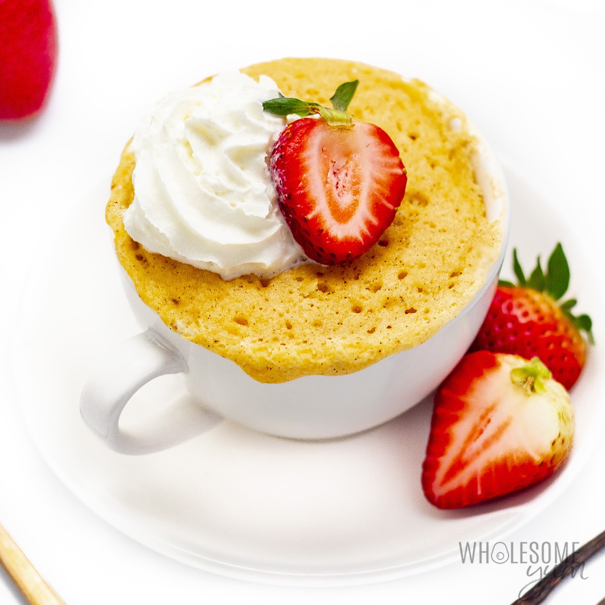 Keto vanilla mug cake with strawberry and whipped cream in a mug. 