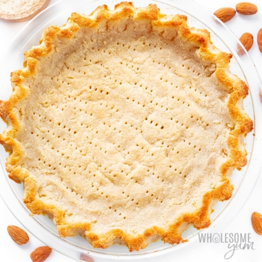 Keto almond flour pie crust with almonds scattered around it.