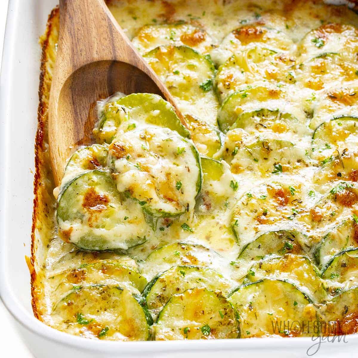 Baked zucchini casserole in a pan with a wooden spoon.