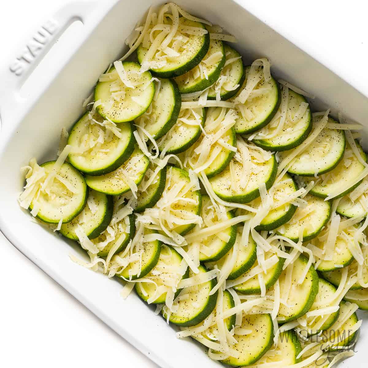 Zucchini layered in casserole dish with shredded cheese.