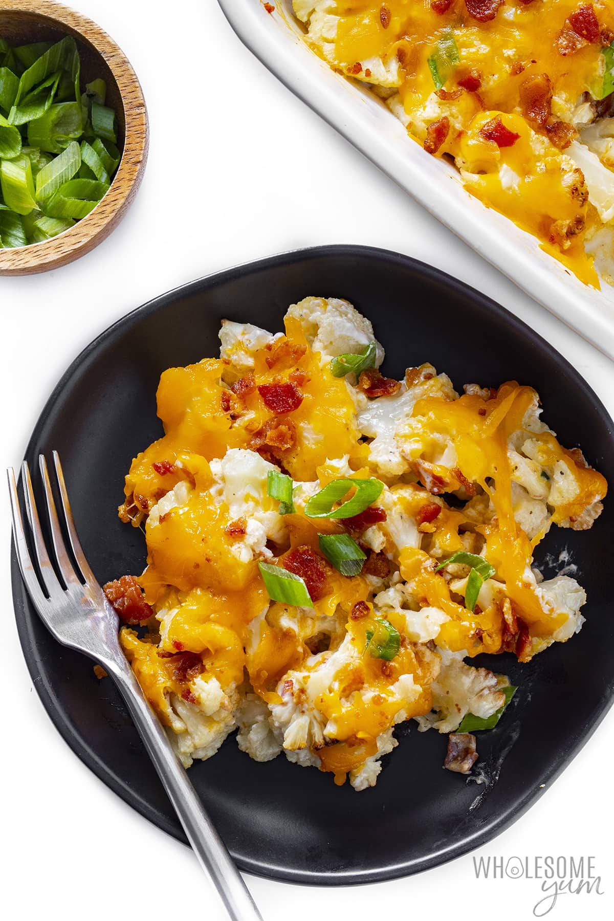 Cheesy loaded cauliflower casserole with a fork on a black plate.