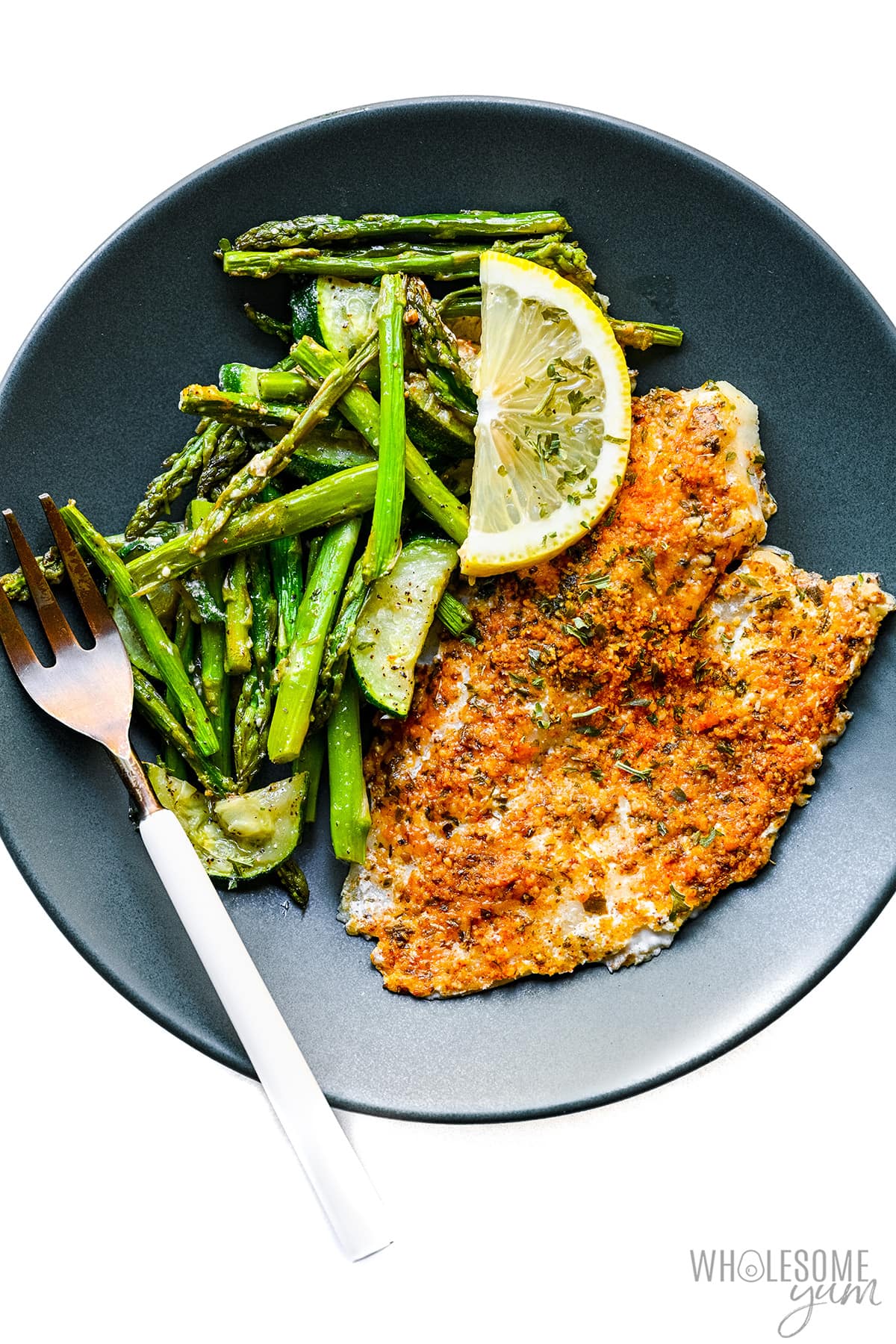 Parmesan tilapia on a plate with asparagus and zucchini.