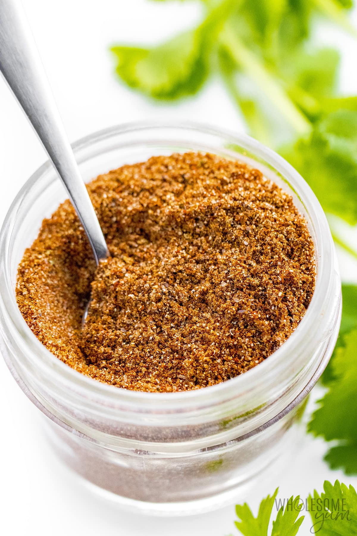 Homemade taco seasoning recipe in a glass jar with a spoon.