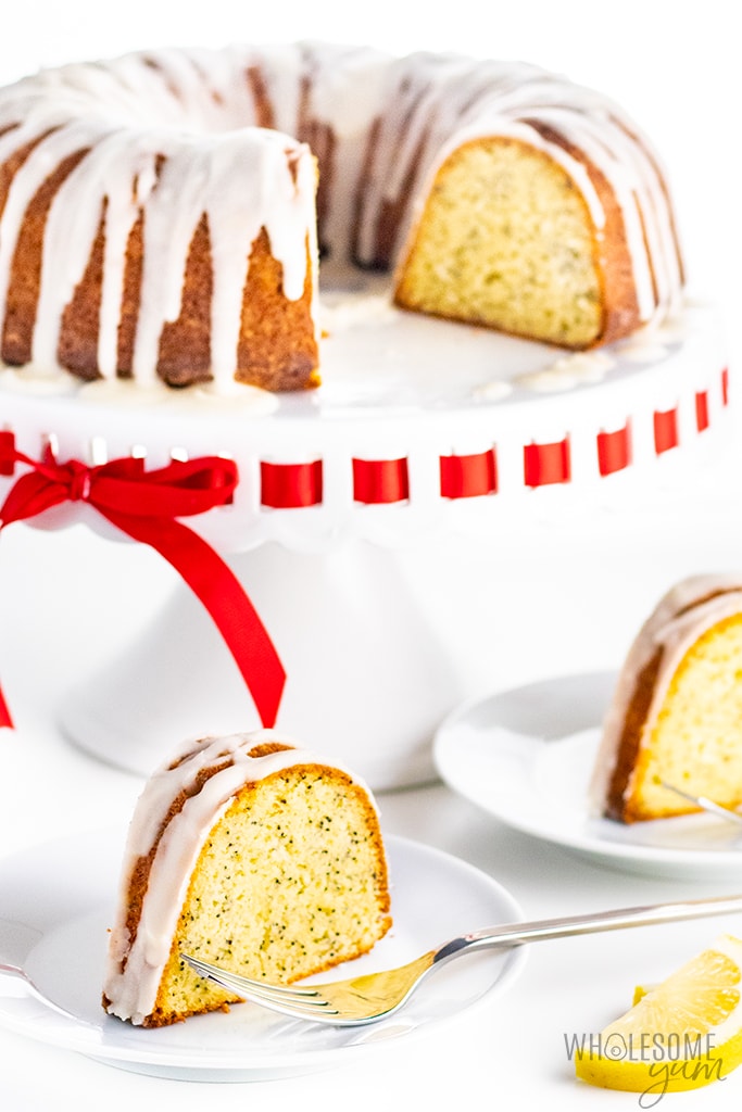 Two slices of low carb lemon pound cake on plates with cake on a stand, closer up