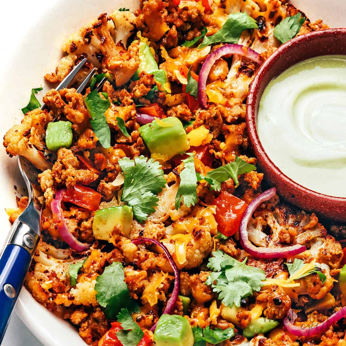 Cauliflower nachos on a plate with sour cream.