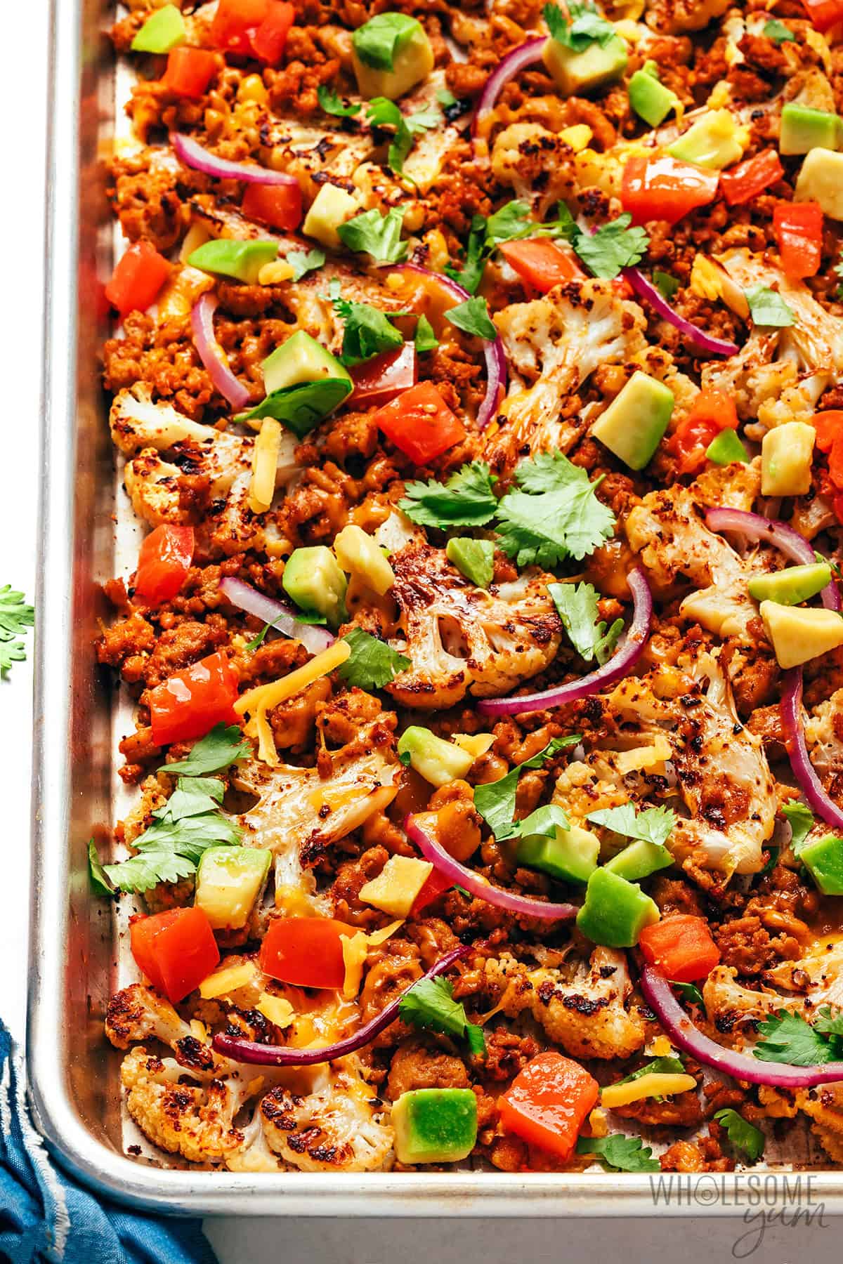 Browned, caramelized cauliflower nachos loaded up with toppings on a baking sheet.