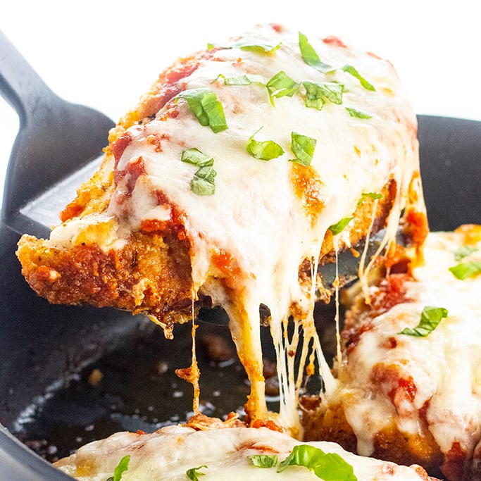 keto chicken parmesan in a pan with one chicken breast on a spatula being removed from the pan
