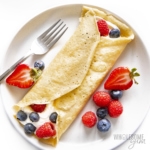 Tomato crepes rolled on a plate with whipped cream and berries on top