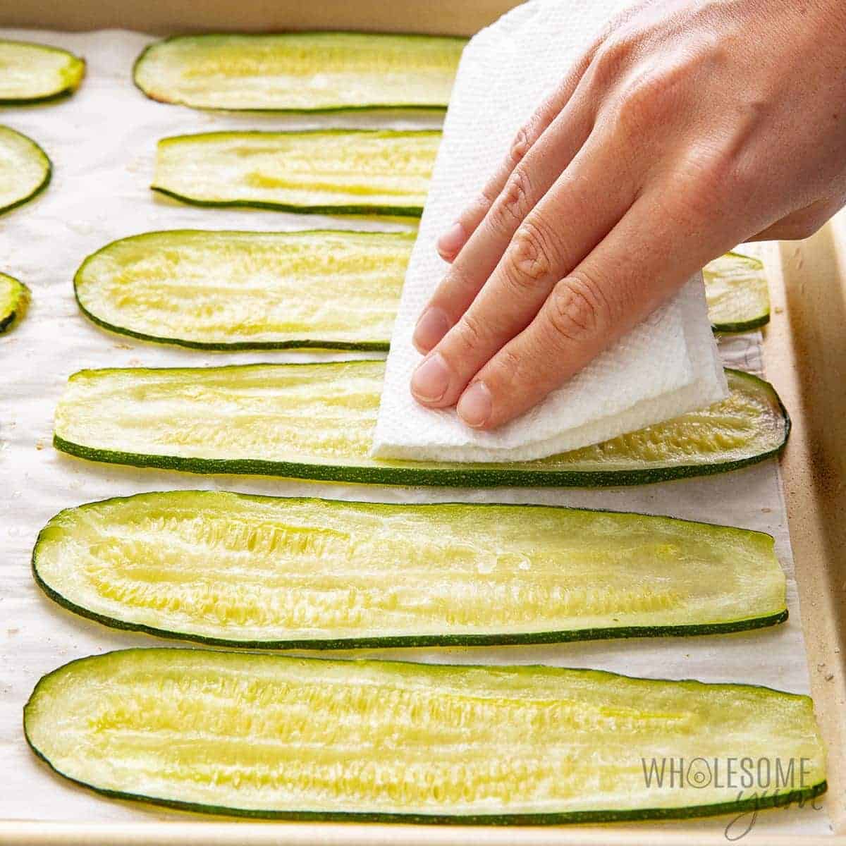 Patting roasted zucchini slices with paper towel.