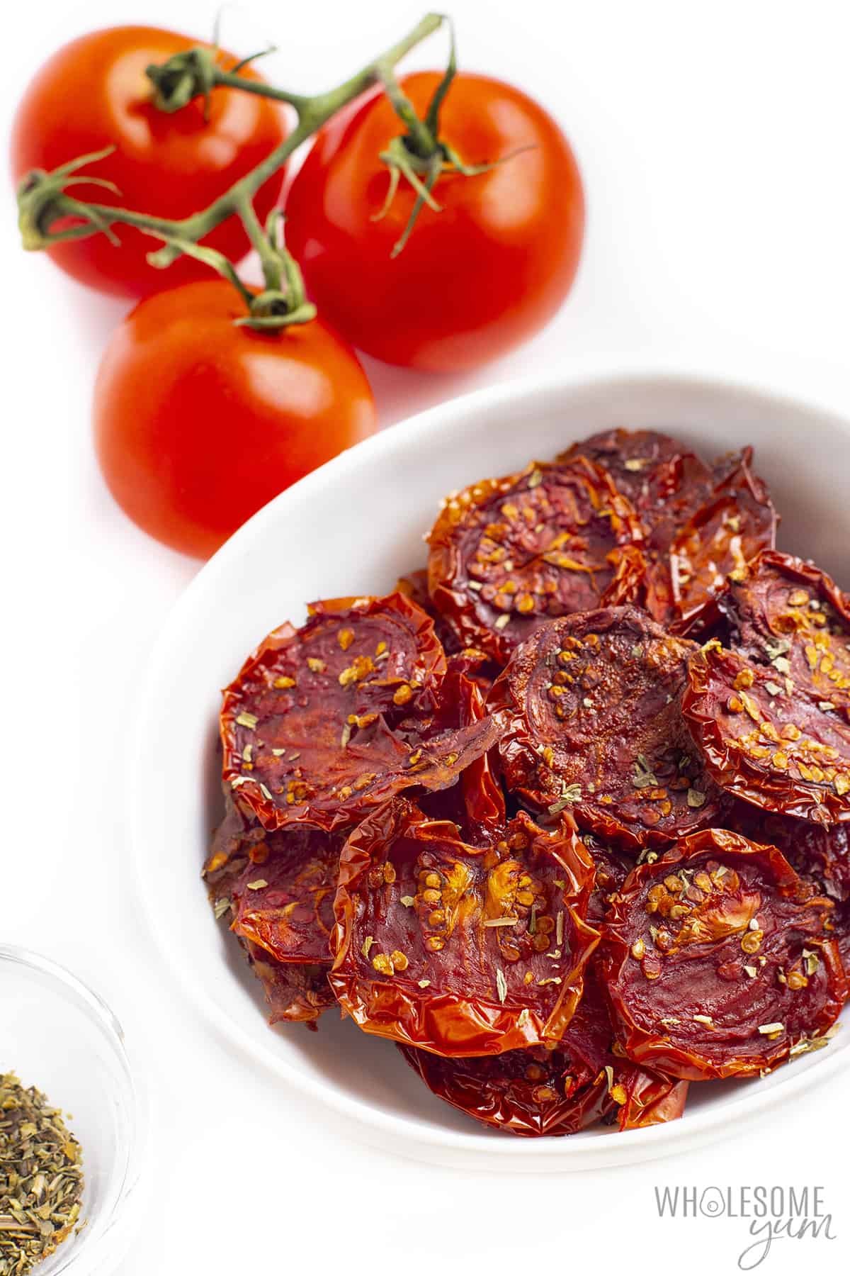 Bowl of sun-dried tomatoes with fresh tomatoes in background.