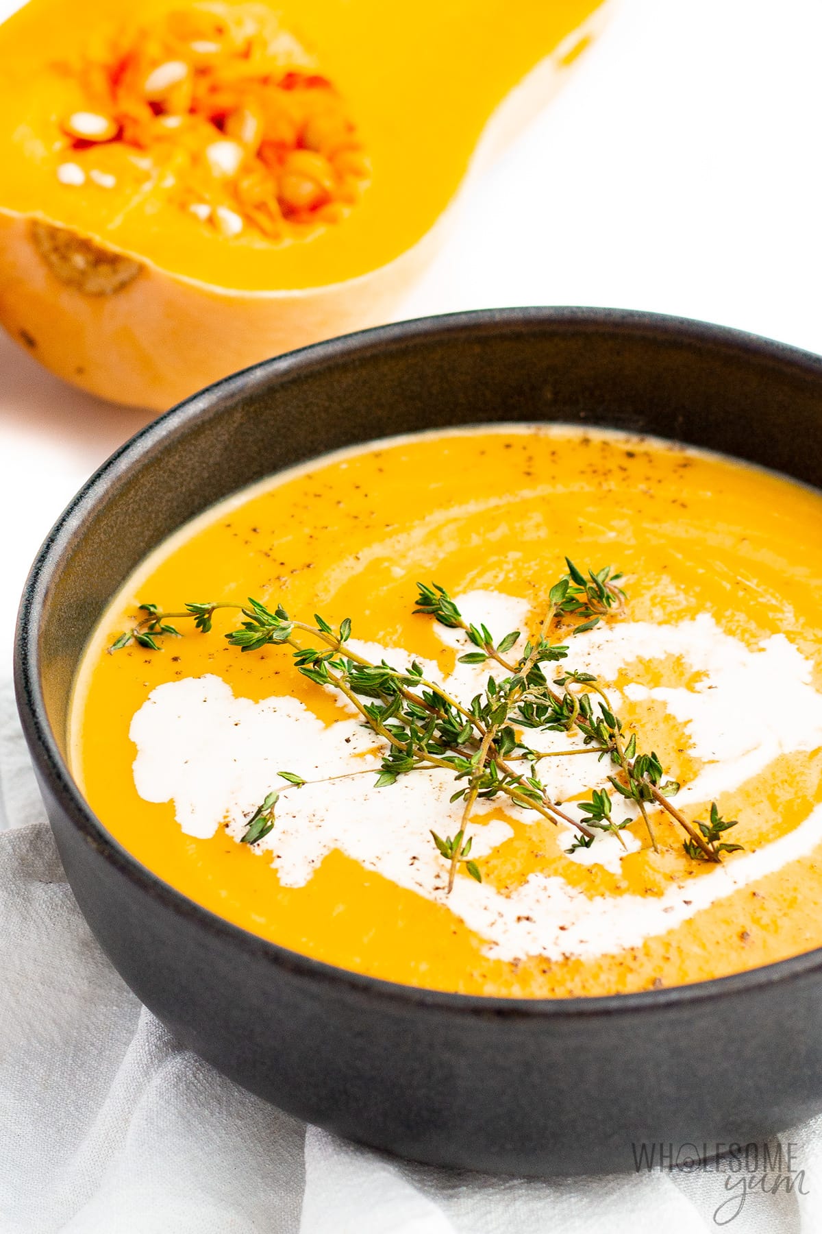 Creamy butternut squash soup with coconut milk drizzle and herb garnish, in a dark bowl.