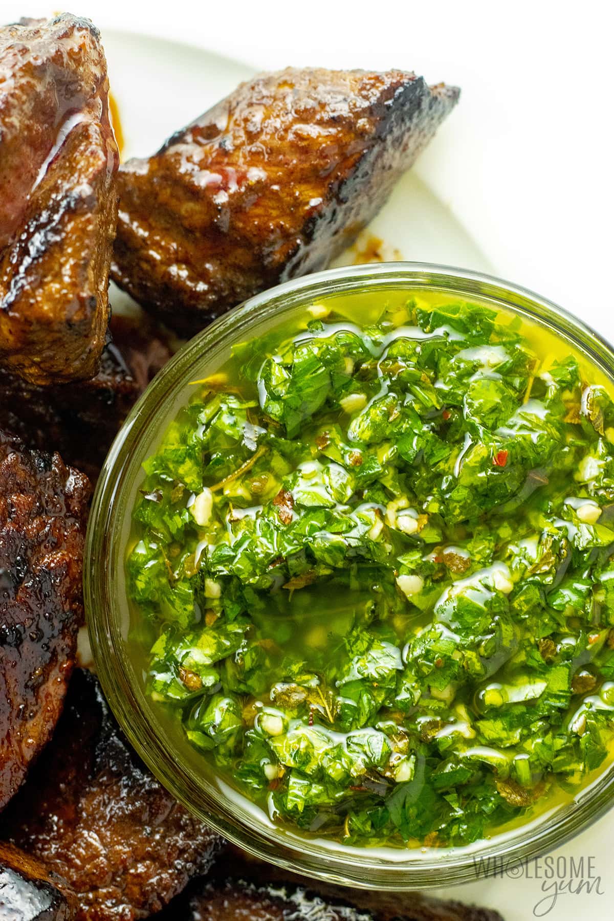 Steak next to chimichurri sauce on a plate.