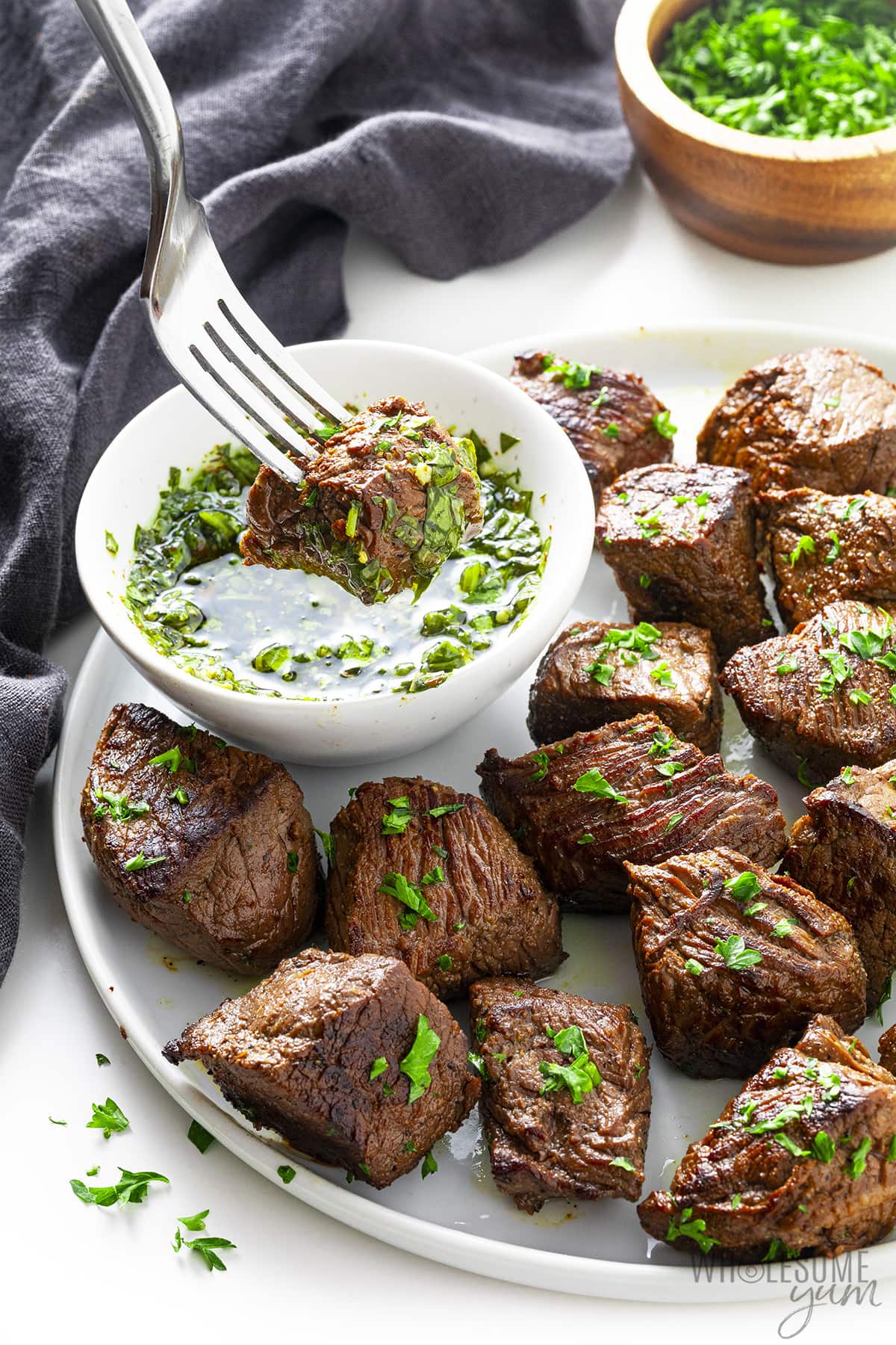 Sirloin steak tips dipped in chimichurri sauce on a plate.