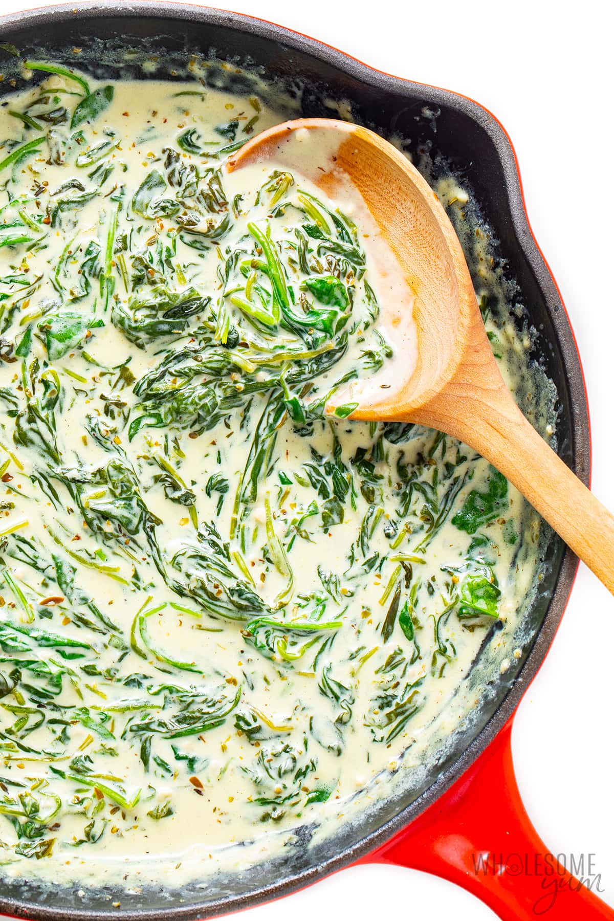 Creamed spinach with cream cheese in a cast iron skillet with wooden spoon.