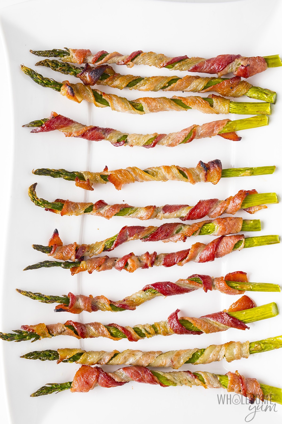 Bacon wraps asparagus on a white plate.
