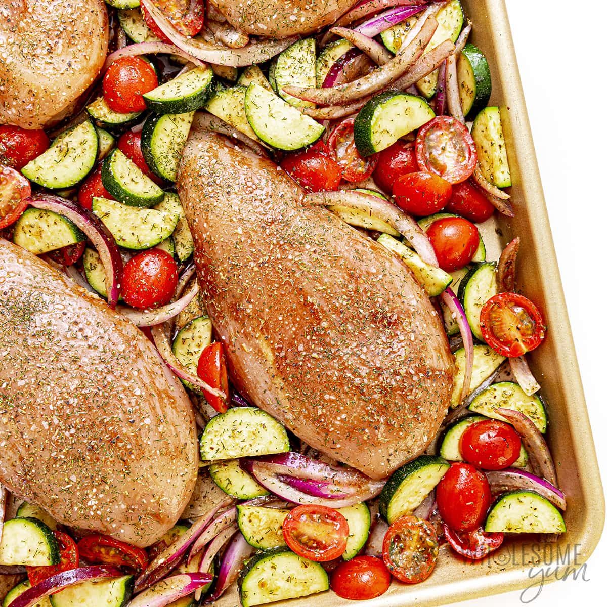 Chicken seasoned and placed between veggies on sheet pan.