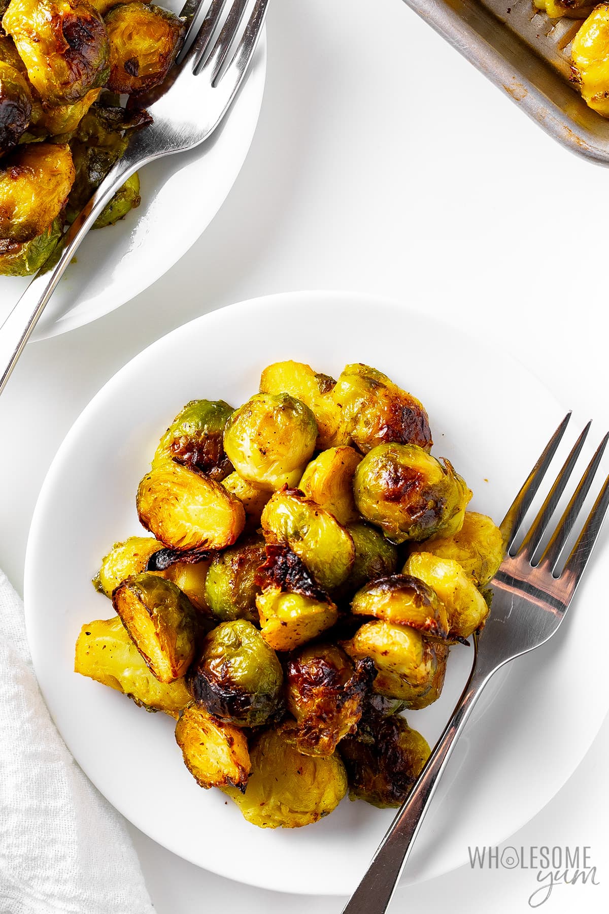 Roasted brussels sprouts on two plates with forks.