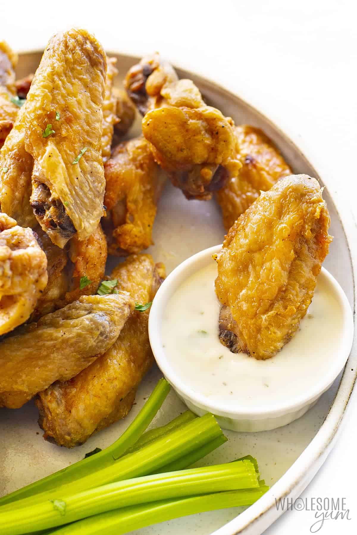 Air fryer wings on a plate with one wing dipped in sauce
