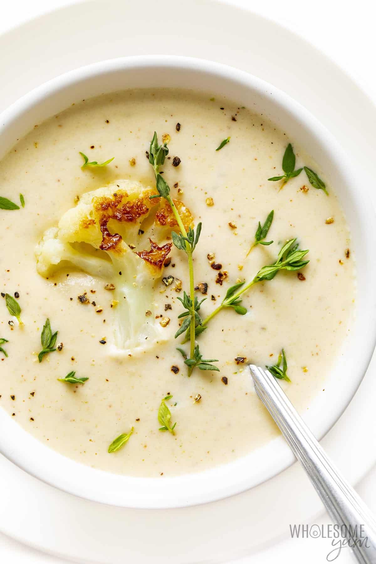 Roasted cauliflower soup in a bowl with spoon and garnishes.