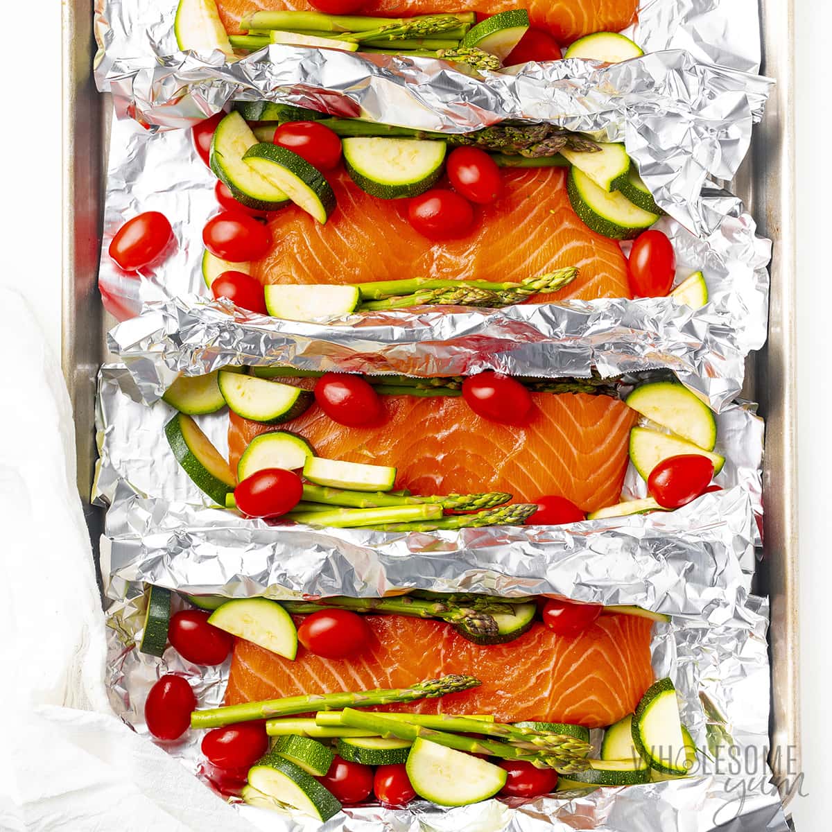 Raw salmon and veggies placed on squares of foil on a baking sheet.