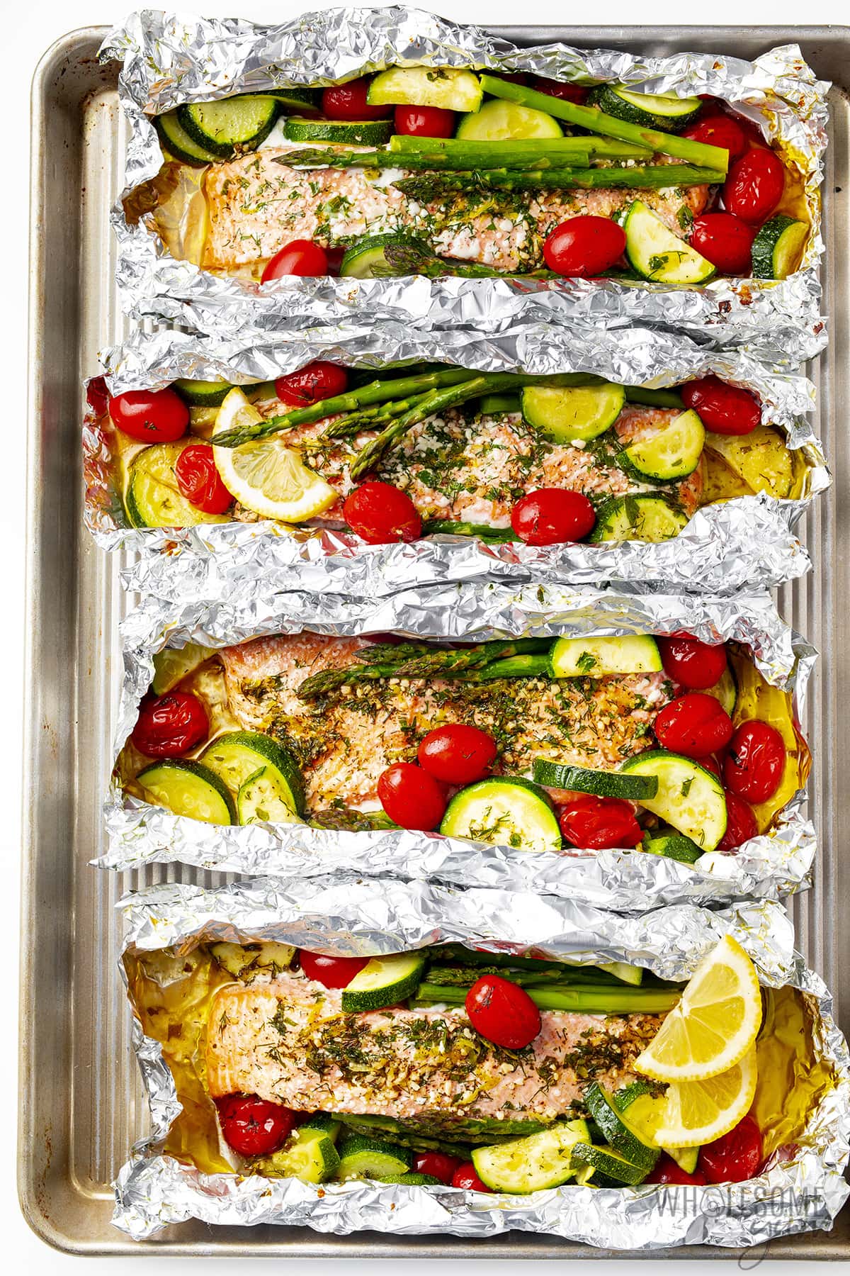 Baked salmon in foil with veggies on a sheet pan.