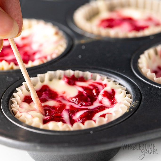 Keto Cheesecake Fat Bombs Process - Swirling raspberry sauce into the mini cheesecakes