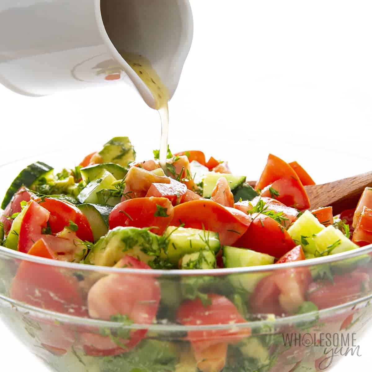 Pouring dressing over salad with tomatoes, avocado, and cucumbers