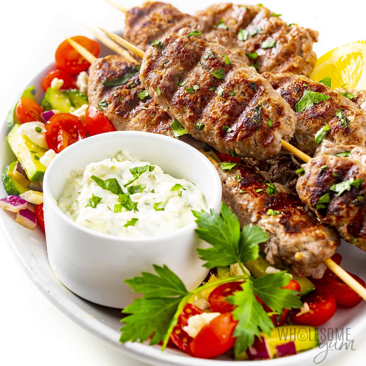 Kofta kebab on a plate next to tzatziki sauce.