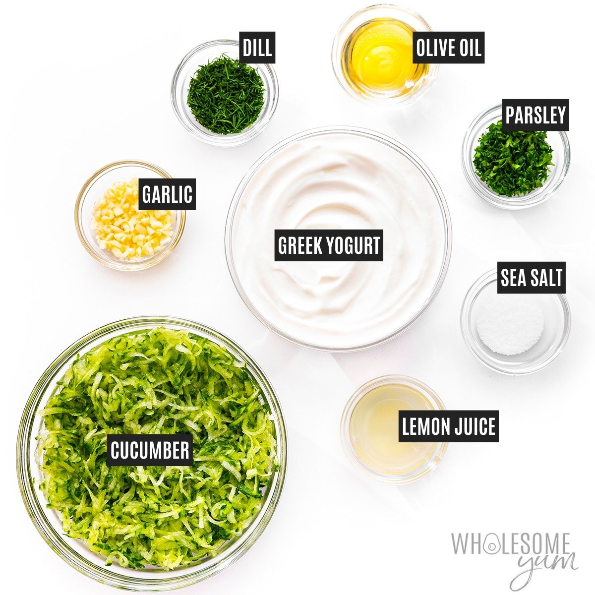 Bowls of grated cucumbers, Greek yogurt, garlic, lemon juice, olive oil, fresh herbs, and salt with labels.