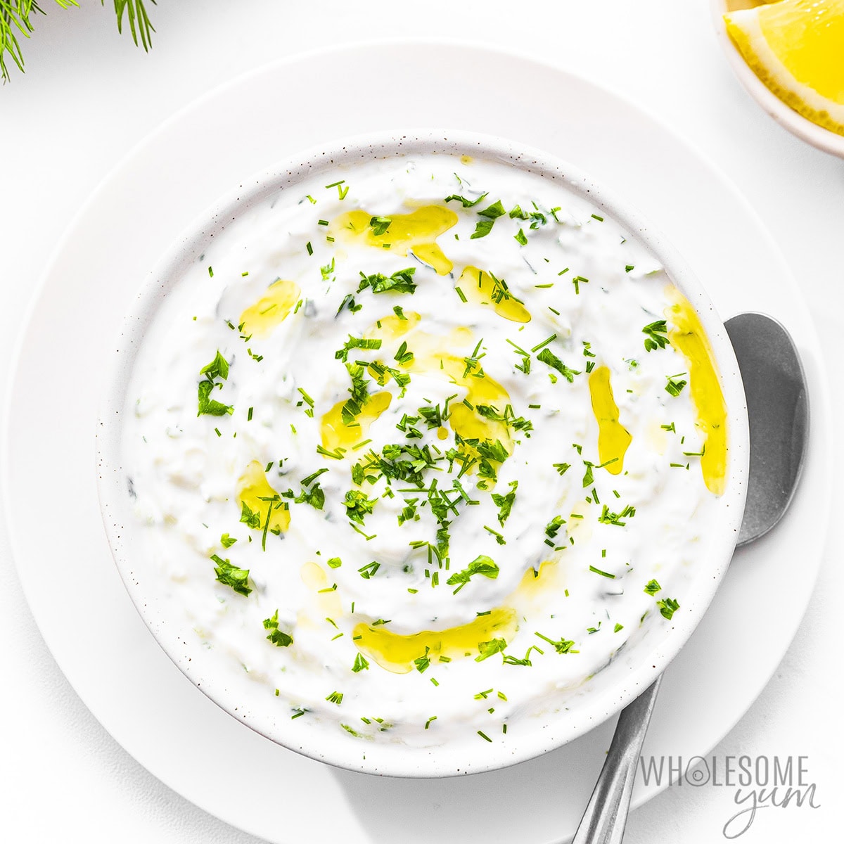 Finished tzatziki sauce recipe in a bowl, garnished with olive oil and fresh herbs.