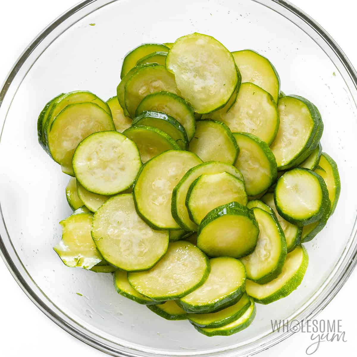 Sliced zucchini tossed with oil and salt in a bowl.