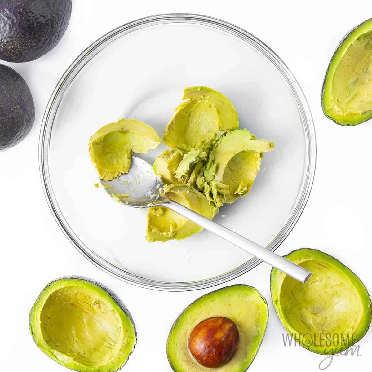 Avocados partially scooped out with flesh transferred to a mixing bowl.