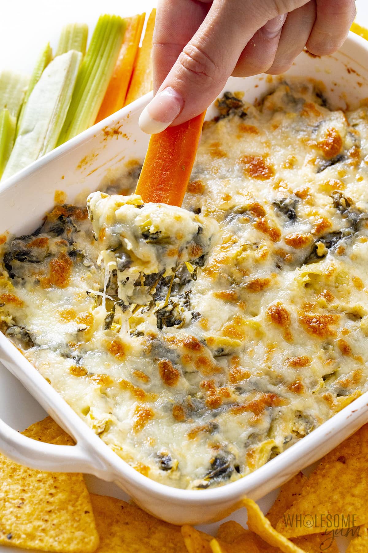 Easy spinach artichoke dip scooped with a carrot stick.