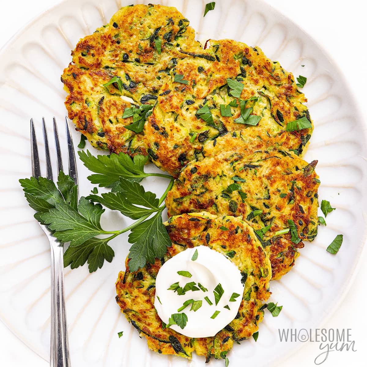 Finished zucchini fritters recipe layered on a plate with a fork.
