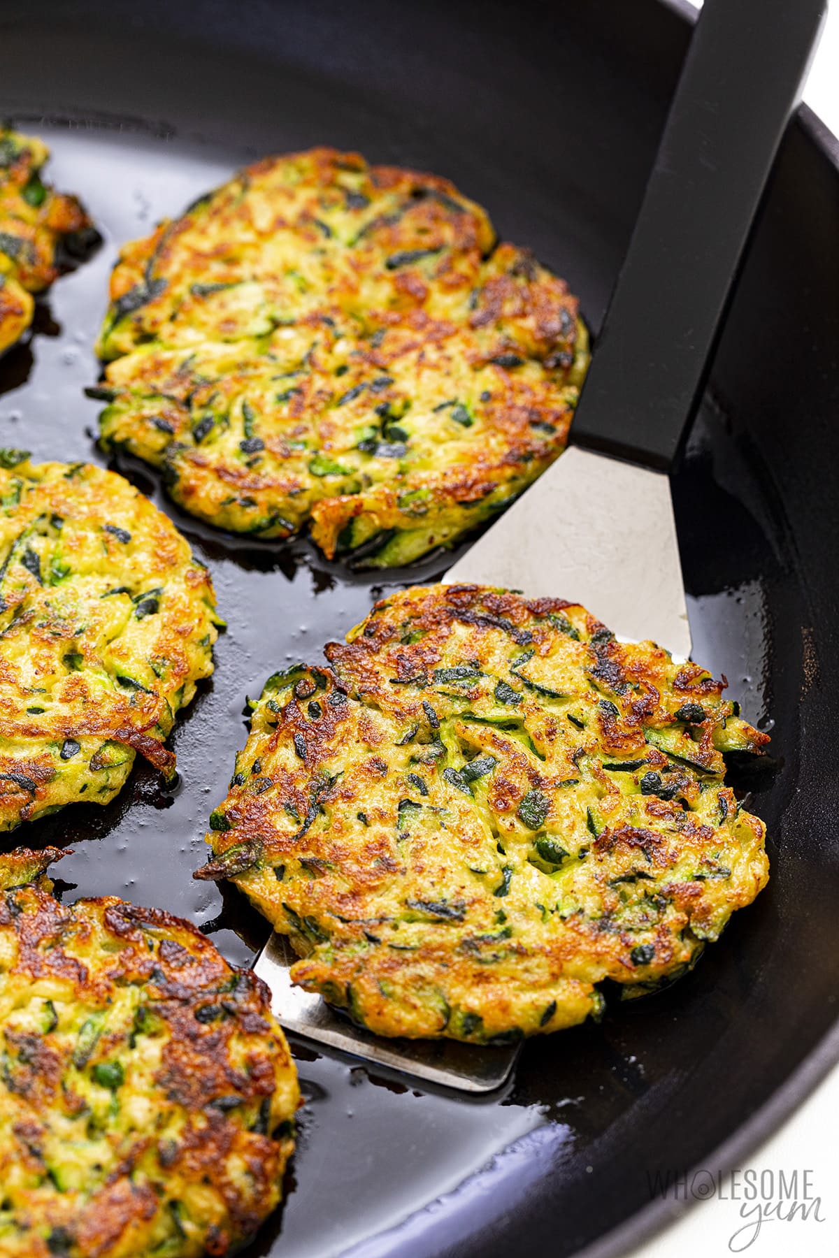 Zucchini fritters recipe lifted out of skillet with a spatula.