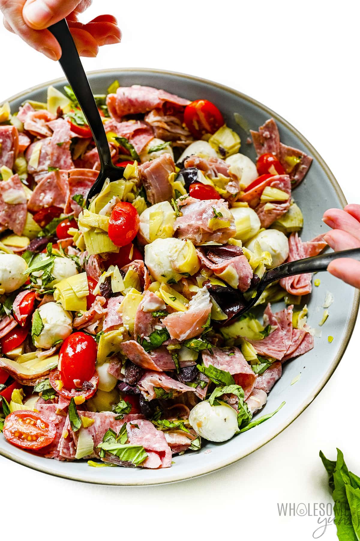 Antipasto salad with serving spoons.