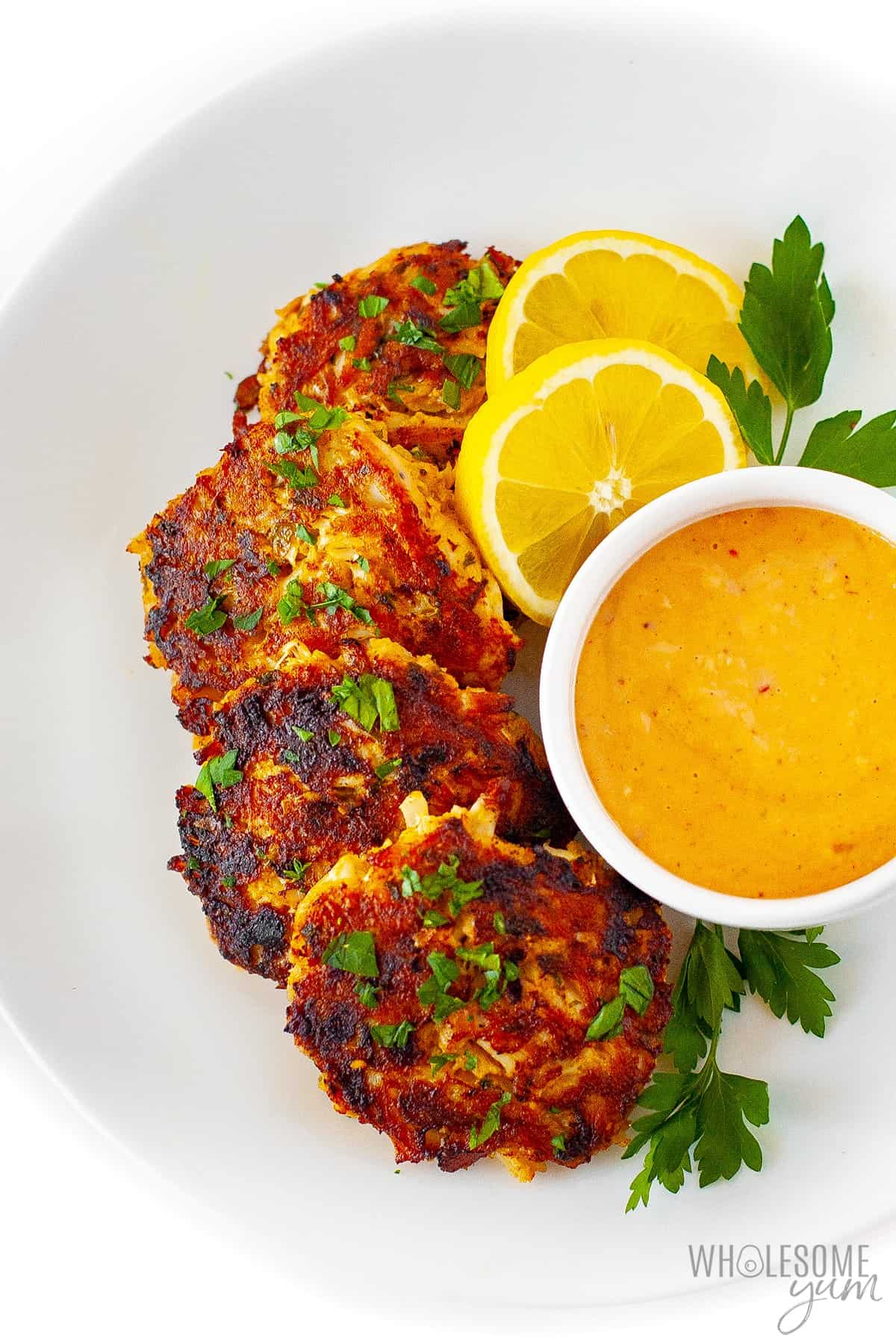 Keto crab cakes recipe on a platter with sauce and lemons.