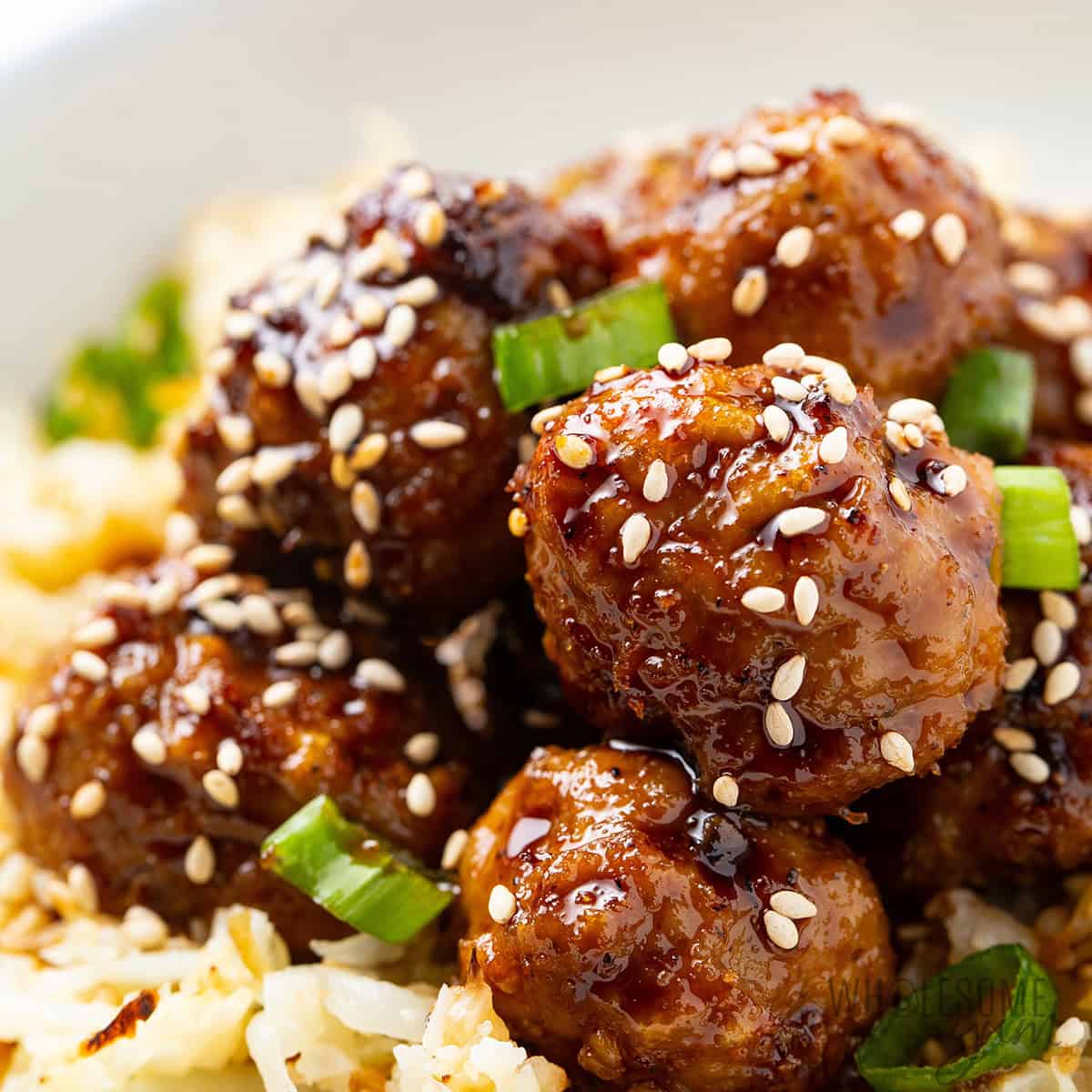 Finished Asian meatball recipe tossed with sauce and garnished with sesame seeds and green onions.