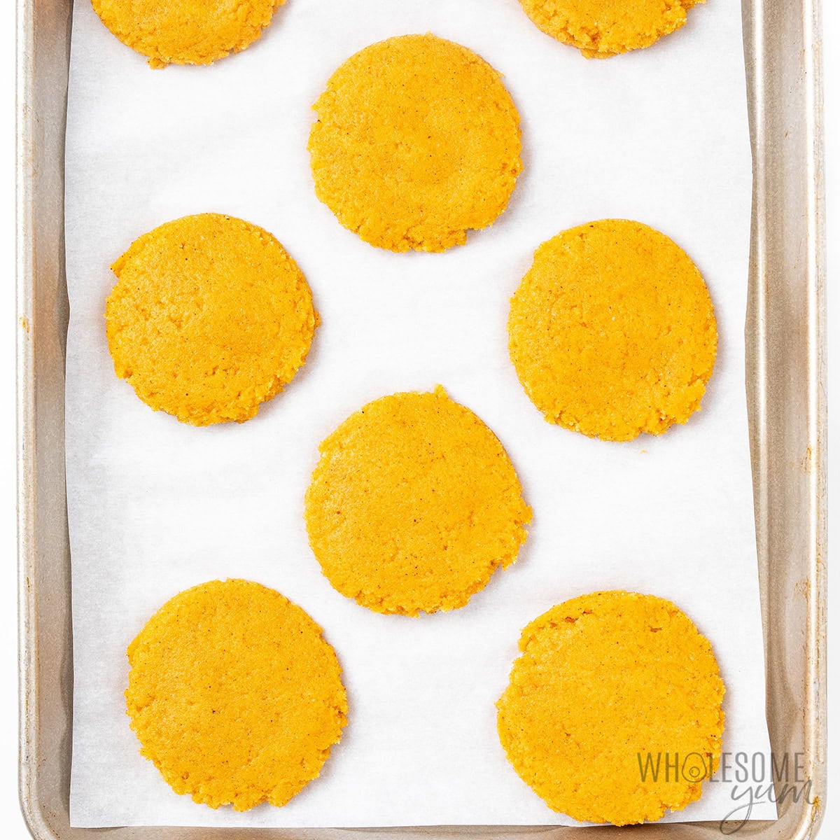 Pumpkin cookies flattened on a lined baking sheet.